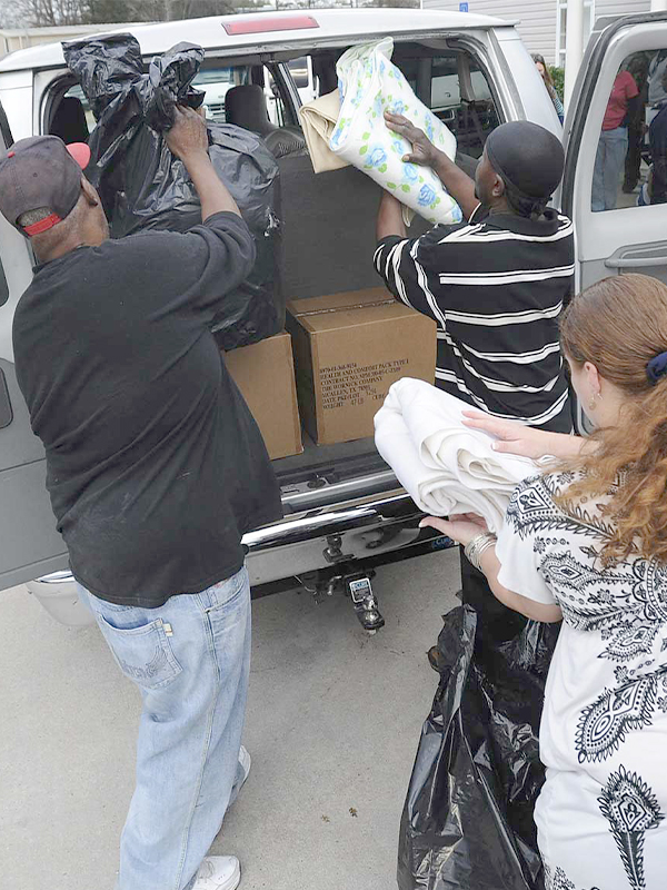 three people putting donations into back of car